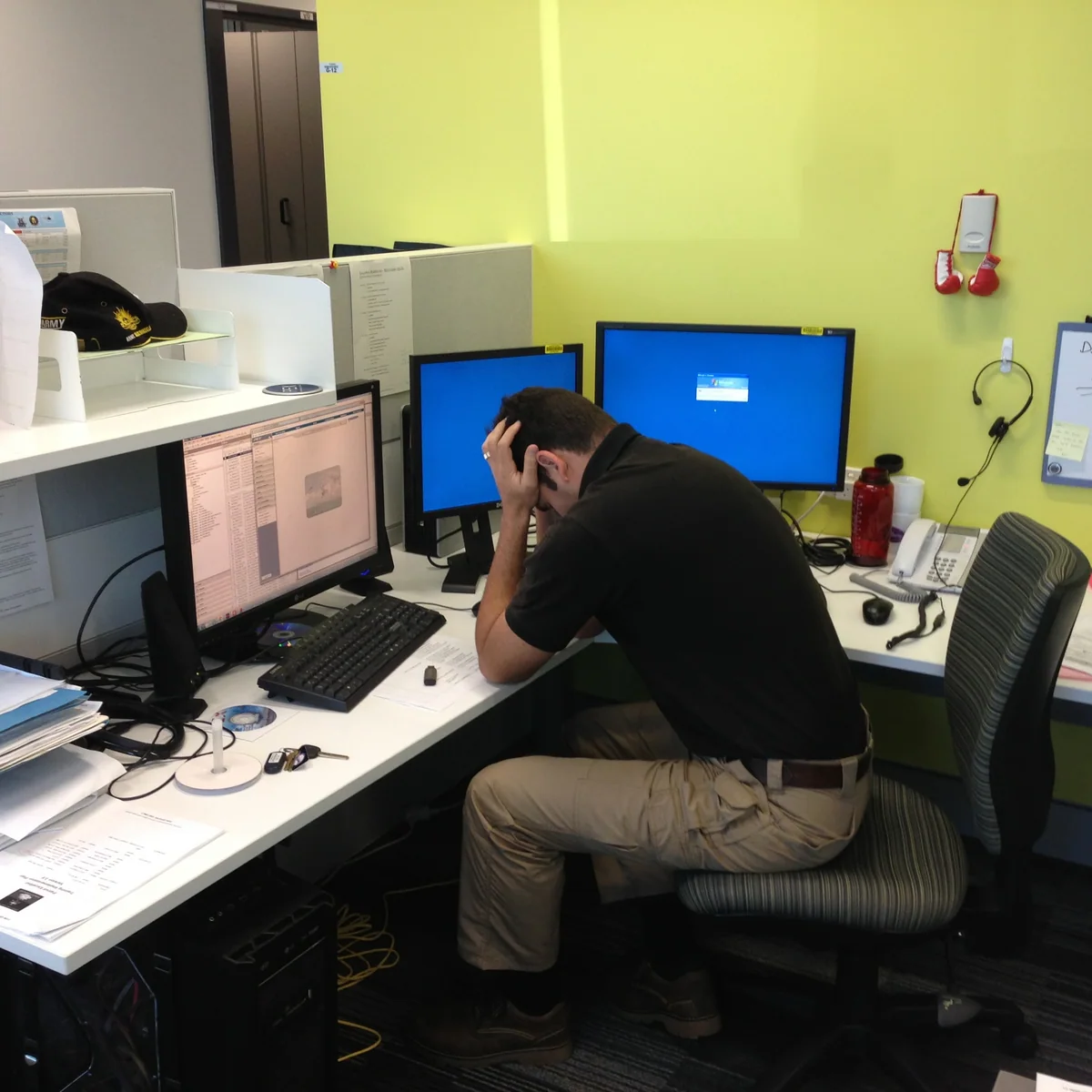 Sean seated at a multi-monitor office desk in Brisbane in 2012, leaning forward with a hand against his head.