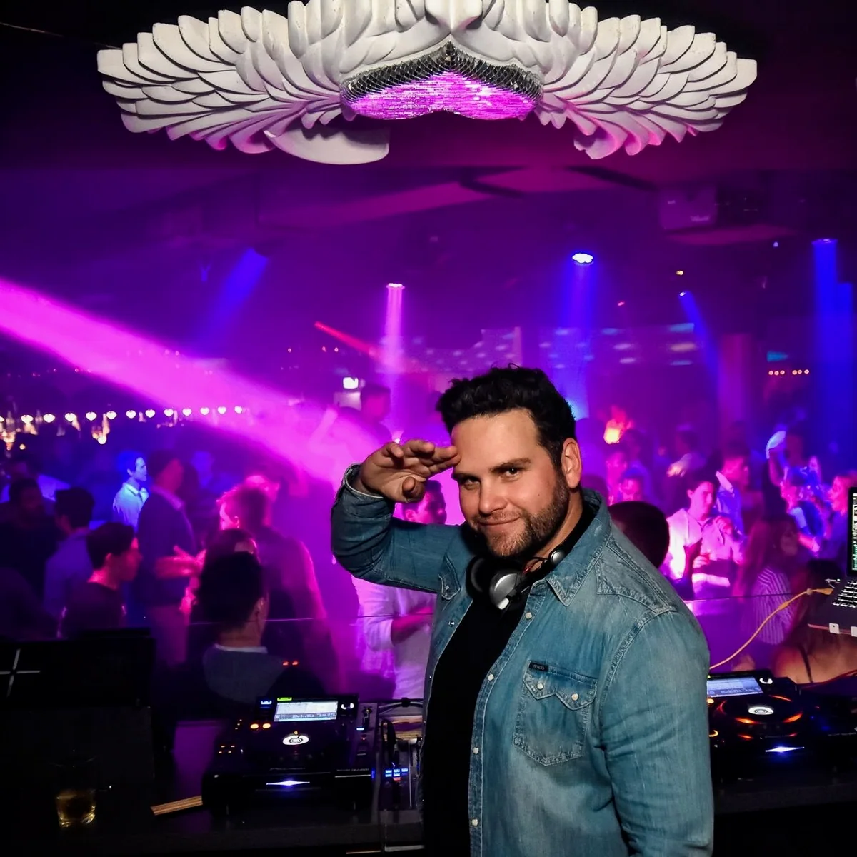 Sean saluting the camera behind the decks at Love Nightclub on the Gold Coast in 2018, with a packed club and purple lights behind him.