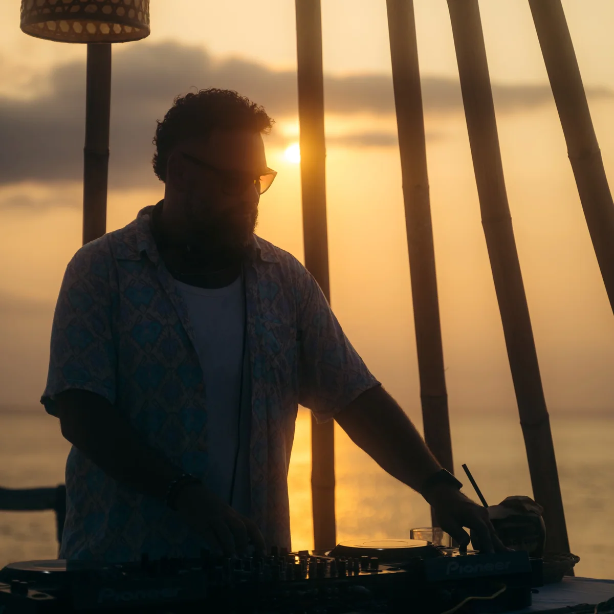 Sean DJing at Suku Bali in 2023, silhouetted against a golden sunset.
