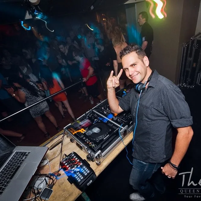 Sean smiling behind DJ equipment with a crowd behind him in Newcastle in 2013.